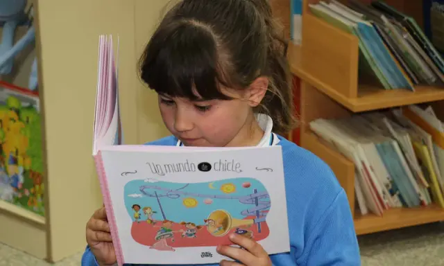 Niña leyendo un libro ilustrado, parte de una colección de libros por edades.