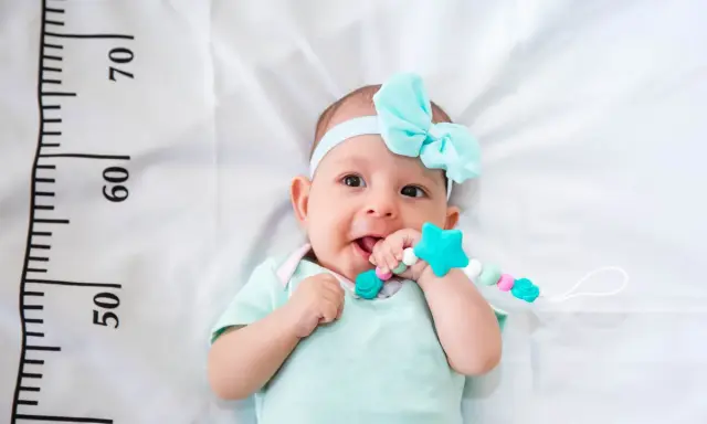 Un bebé sonriente con un chupete de estrella turquesa, con una cinta azul en la cabeza. A su lado, una regla marca el crecimiento, ¡un bebé perceptible!