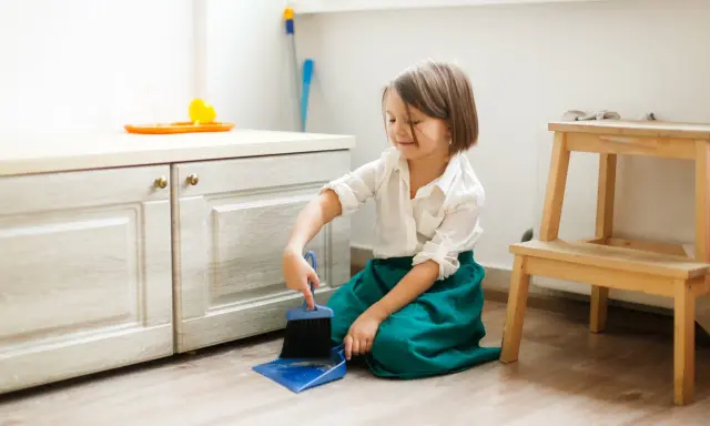 Niña practicando vida práctica Montessori, barriendo el suelo con escoba y recogedor.