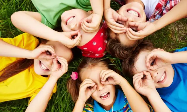 Niños riendo y jugando en el césped, creando formas con sus manos. Sonrisas contagiosas, perfectas para frases para niños.