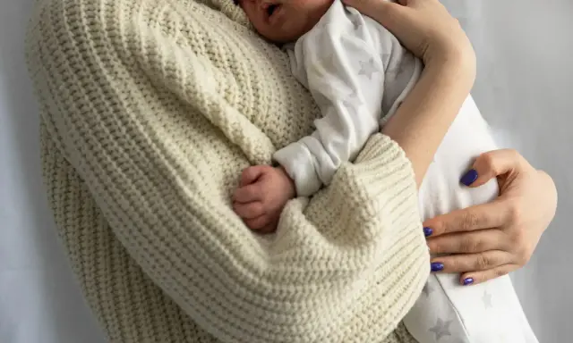 Bebé durmiendo acurrucado en brazos de su madre, envuelto en un suéter tejido. Un recordatorio de cuanto duerme un recién nacido.