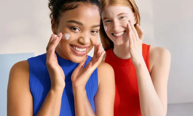 Dos mujeres sonríen mientras aplican crema en sus rostros. Piel con piel hasta cuando, la belleza natural se realza con cuidado.