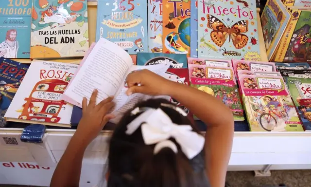 Niña lee libros sobre cuentos de igualdad de género, rodeada de coloridas portadas que inspiran a la imaginación.