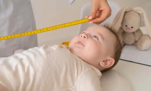 Bebé de 20 meses siendo medido con cinta métrica. Un peluche de conejo observa atentamente.