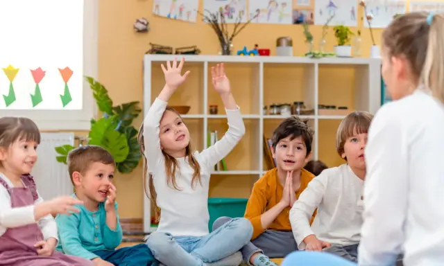 Niños atentos en clase, quizás buscando frases para profesores despedida. Una niña levanta la mano, ansiosa por participar.