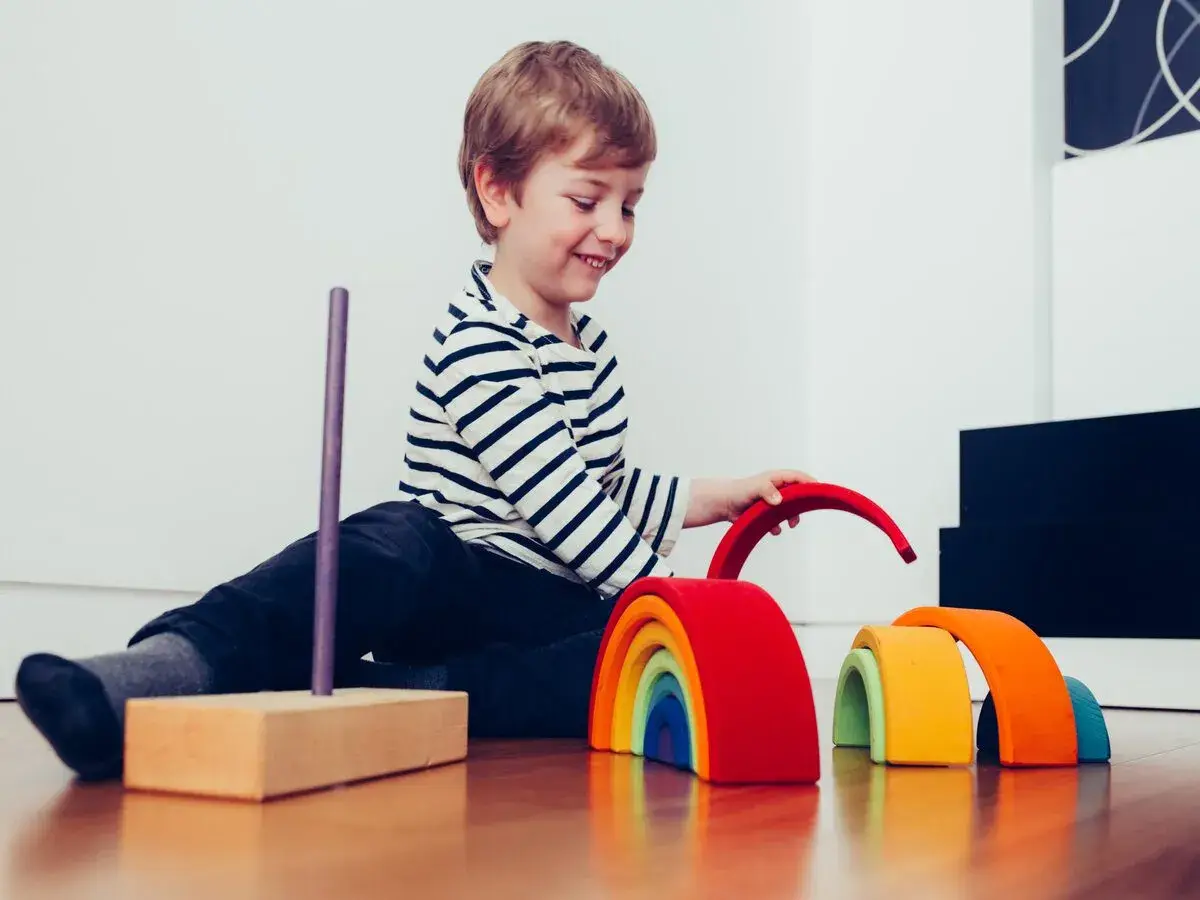 Niño sonriente juega con bloques de madera de arcoíris, un ejemplo de la pedagogía Waldorf que fomenta la creatividad y el desarrollo.