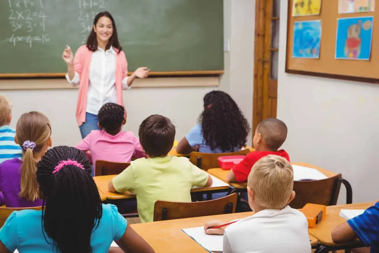 Un buen profesor explica matem&aacute;ticas en la pizarra a una clase atenta. Los ni&ntilde;os toman notas y escuchan.