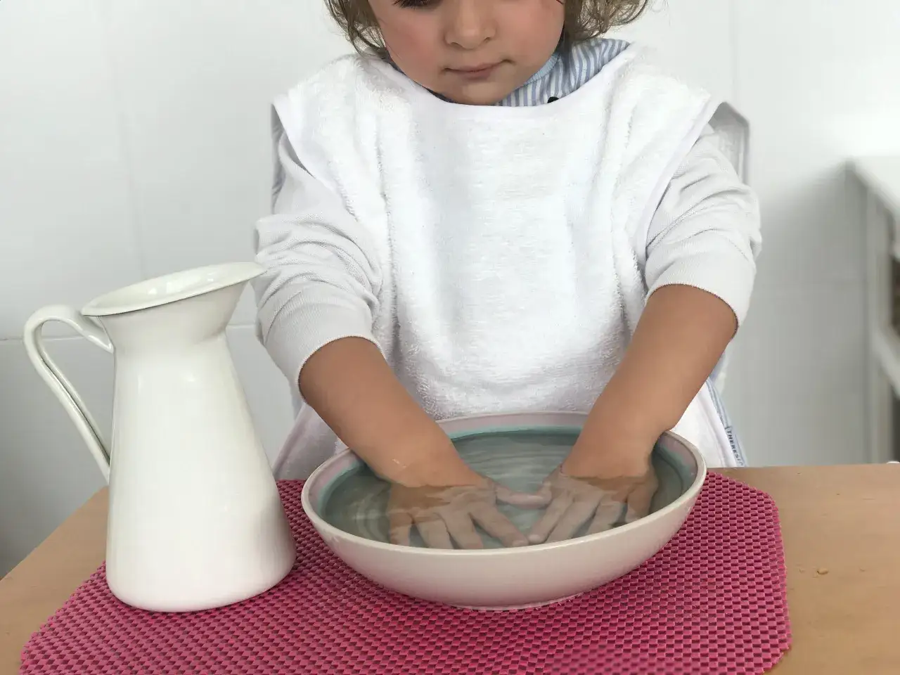 Ni&ntilde;o concentrado realizando actividades m&eacute;todo Montessori: lavado de manos con jarra y cuenco.