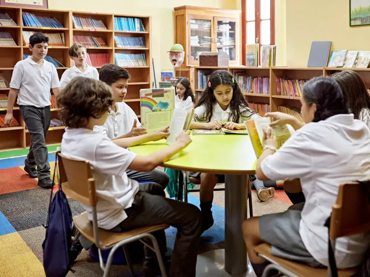 Niños de 10 a 12 años en una biblioteca escolar, rodeados de estanterías llenas de libros, comparten lecturas y descubren nuevas historias.