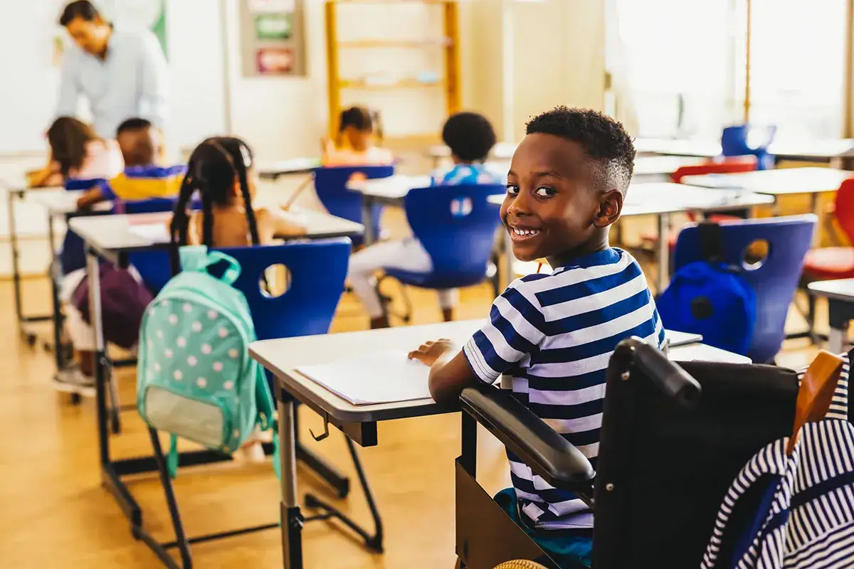 Ni&ntilde;o sonriente en silla de ruedas en aula. Su perfil de salida muestra optimismo y ganas de aprender.