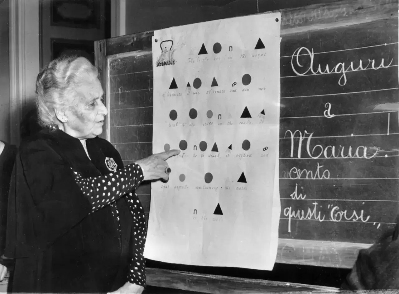 Joven Maria Montessori señala un gráfico con formas y texto. En la pizarra, 