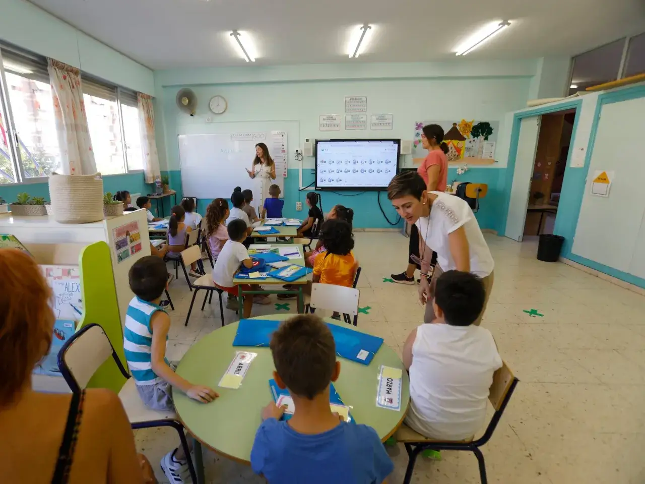 Ni&ntilde;os y maestros interact&uacute;an en un aula luminosa, promoviendo un ambiente de colegio inclusivo donde todos aprenden juntos.