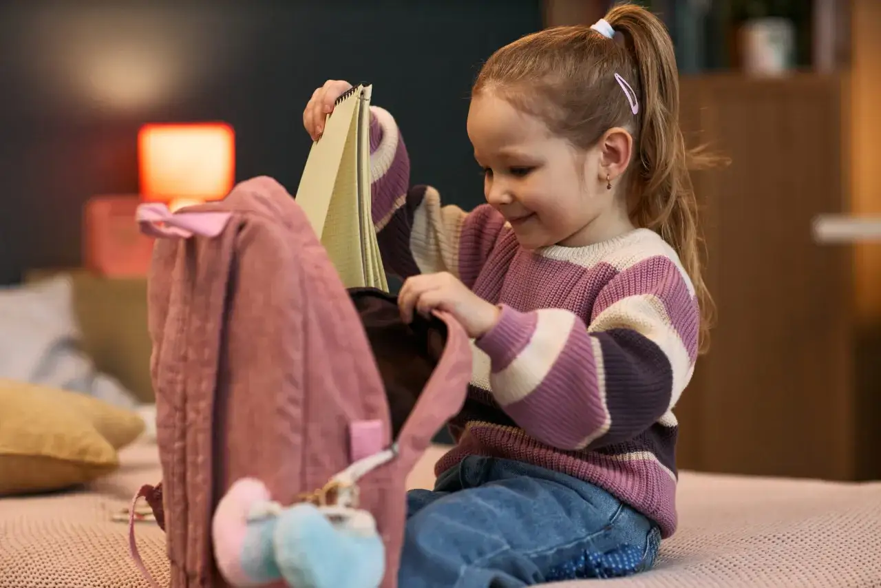 Ni&ntilde;a guarda cuaderno en mochila rosa. Un ejemplo de actividades de la vida diaria, prepar&aacute;ndose para la escuela o una aventura.