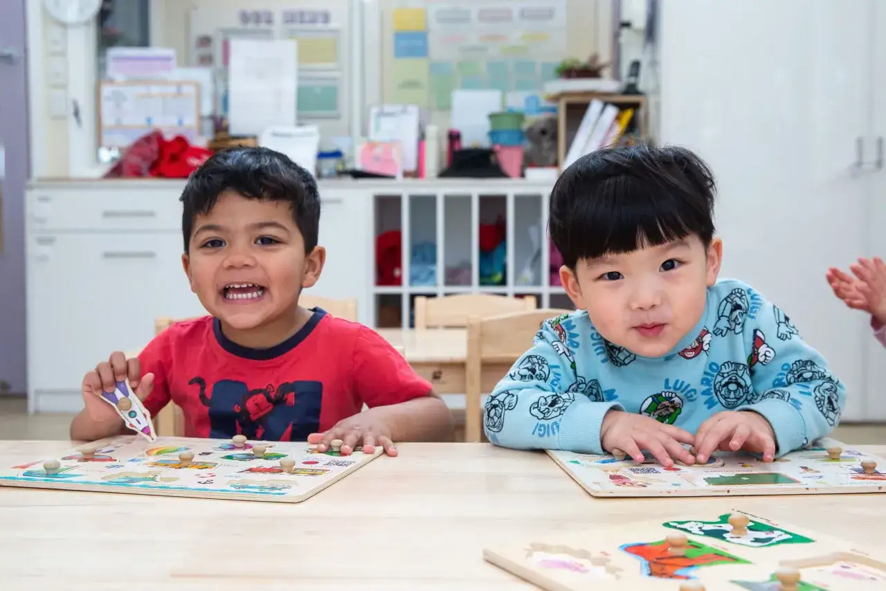 Dos ni&ntilde;os peque&ntilde;os juegan con rompecabezas de madera, aprendiendo y divirti&eacute;ndose. Son frases de educaci&oacute;n para ni&ntilde;os, fomentando el desarrollo.