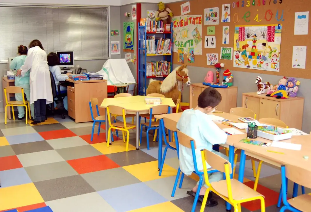 Aula de atenci&oacute;n educativa con ni&ntilde;os y educadores, mesas, sillas de colores y material did&aacute;ctico.