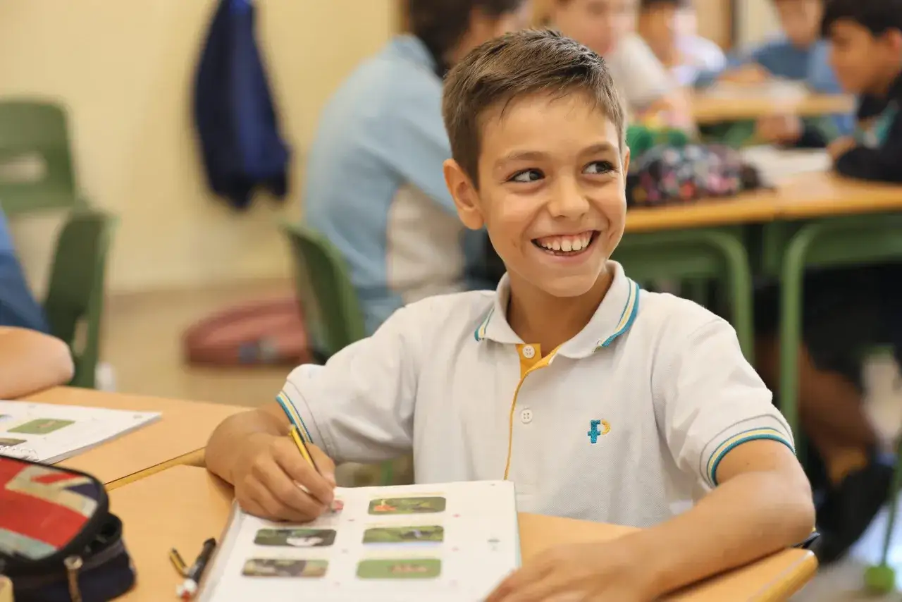 Ni&ntilde;o sonriente en clase, aprendiendo con un libro. Un d&iacute;a perfecto para frases de bienvenida al colegio.