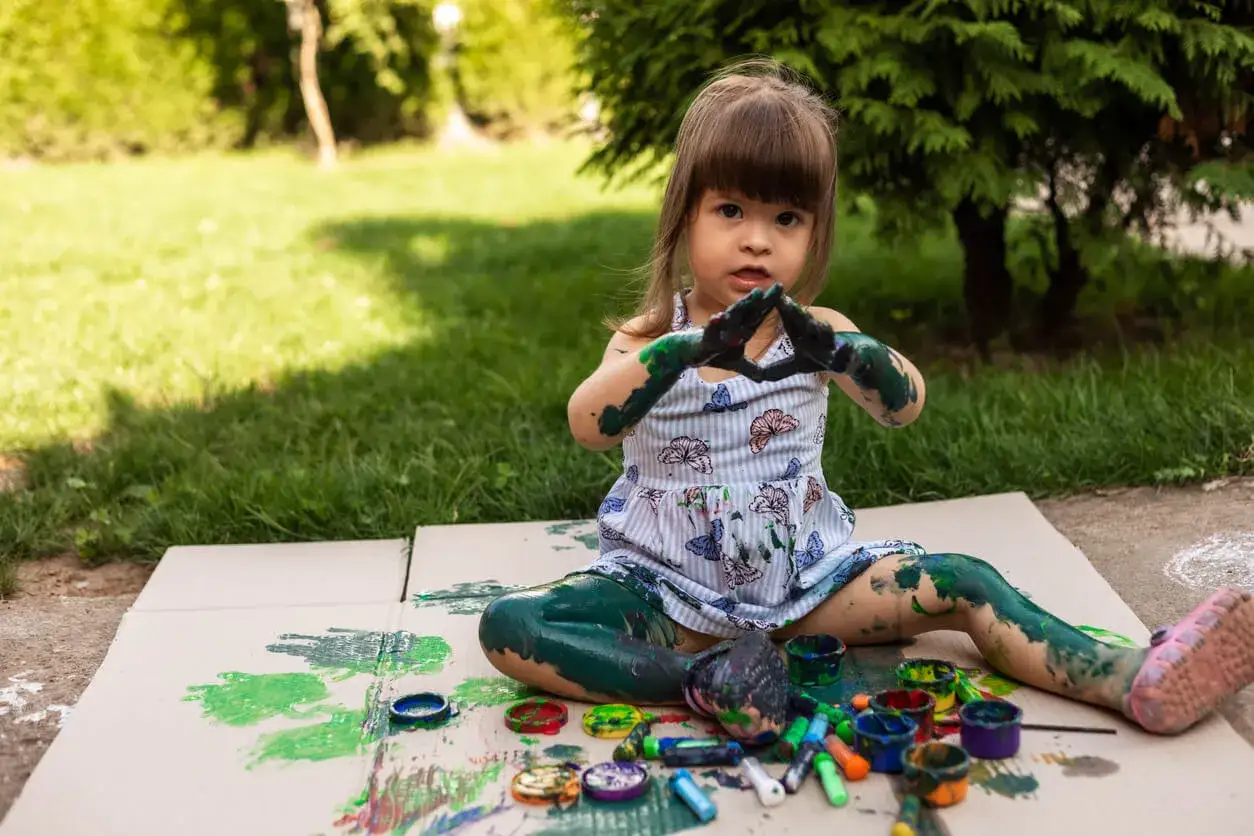 Ni&ntilde;a cubierta de pintura verde, con las manos en forma de coraz&oacute;n, experimentando con el m&eacute;todo Steiner al aire libre.