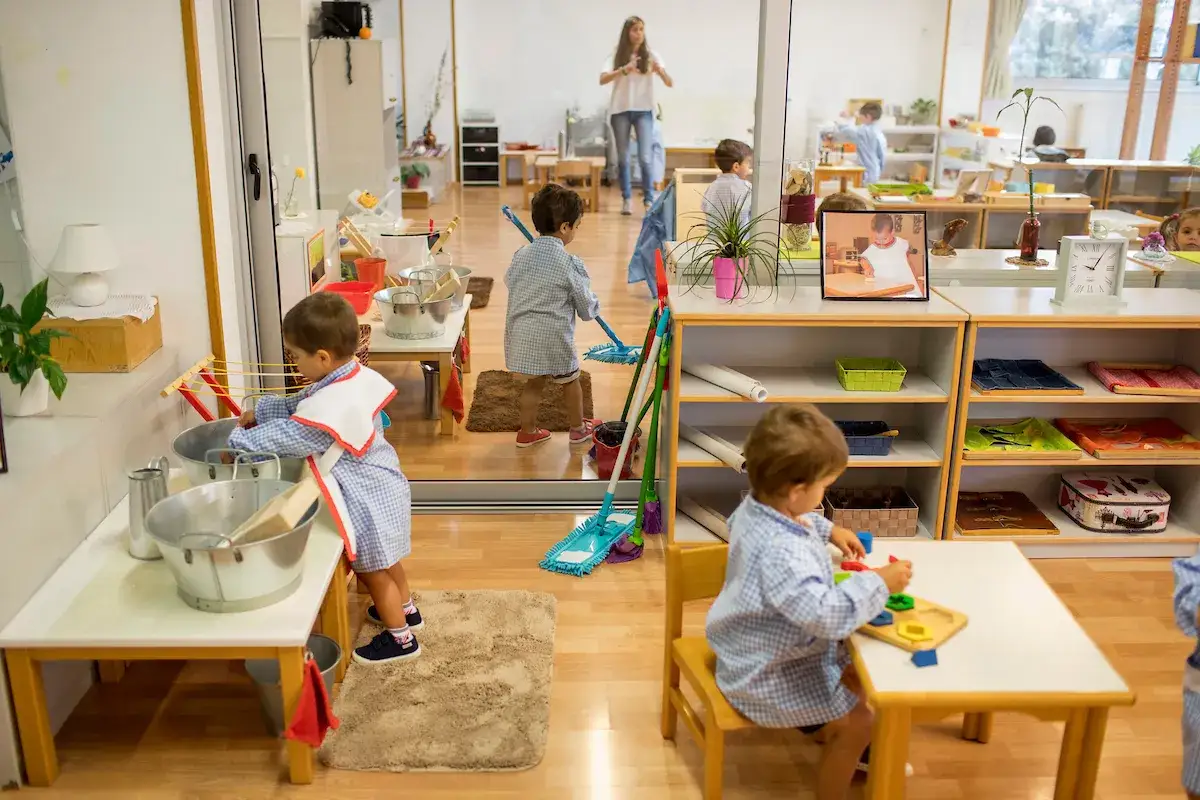 Ni&ntilde;os aprendiendo con una gu&iacute;a Montessori: uno lava, otro barre, y otro juega con bloques.